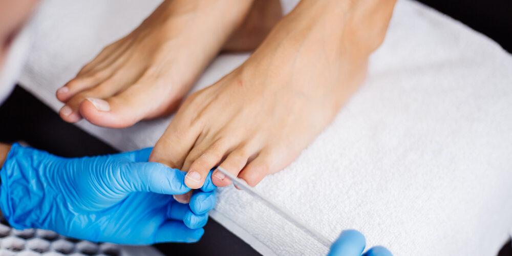 Soin des pieds par un professionnel avec gants bleus sur serviette blanche.